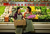 Frauen mit Gemüsekisten vor Gemüseregal in einem Supermarkt