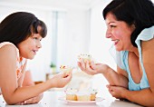 Hispanic mother and daughter eating cupcakes
