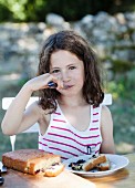 Mädchen isst Brombeerkuchen im Garten