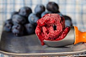 Plum sorbet in an ice cream scoop in front of fresh plums
