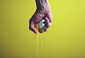 Hand Crushing Raw Egg on Yellow