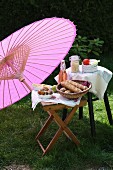 Picnic of bread rolls and lemonade under Oriental paper parasol in garden