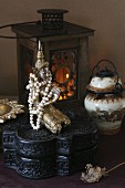 Bead necklace on Buddha figurine on carved, black wooden box and Chinese vase in front of lit candle lantern