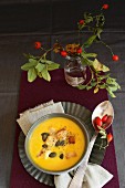 Cream of pumpkin soup with pumpkin seeds and a sprig of rosehips decorating the table