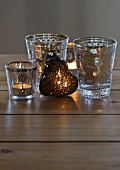 Lit tealights in Oriental tea glasses and heart-shaped ornament on wooden surface