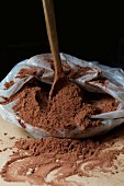 A wooden spoon in a plastic bag of cocoa powder