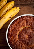 Banana cake in the baking tray with some raw bananas on the left