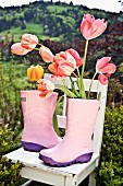 Rosa Gummistiefel auf Gartenstuhl mit Tulpen