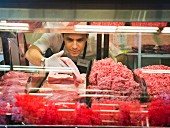 A sales assistant taking meat from the sales display in a butchers