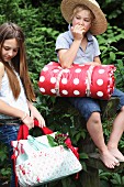 Children outdoors with picnic bag and rolled blanket with red and white polka dot pattern