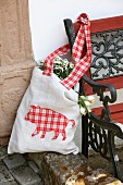 Cloth bag with appliqué, gingham animal motif hanging on garden bench