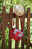 Straw hat & handbag with appliqué red stag motif hanging on wooden fence