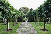 Baumreihen neben gepflastertem Weg und formgeschnittene Buchsbäume in englischem Garten