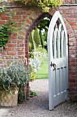 White, wooden, Gothic-style open garden gate in brick wall with view of topiary box trees beyond