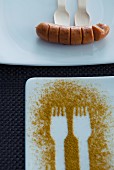 Fork prints in curry powder on a plate and a sausage