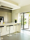 Zeitgenössische offene Küche mit grauem Fliesenboden & Barhockern an Frühstückstheke, seitlich offene Falttür mit Blick auf Terrasse