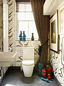 Large tiles with floral pattern in bathroom with draped curtains & collection of retro vases next to toilet