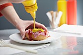 A person squirting ketchup and mustard on a doughnut
