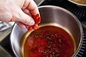 A hand puts paprika powder into a pot for paprika sauce