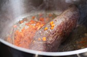 pieces of carrots and onions frying with a tenderloin beef in a pot, for a typical Czech dish called Svickova