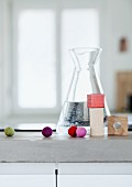 Colourful felt balls and building blocks in front of carafe of water on concrete kitchen worksurface