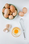 Frische Eier in einer Schüssel, aufgeschlagenes Ei und Schneebesen