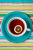 Cup of Tea With Slice of Lemon on Blue Plate and Striped Tablecloth, High Angle View
