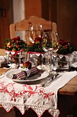 Place setting with linen napkin and wine glass in front of Christmas arrangement on embroidered runner