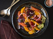 Citrus salad with grapefruit, orange, lime, mint and red onions in a dark stoneware plate with silver utensils on a dark surface