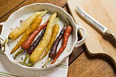 Roasted multi-color carrots in a white scalloped dish with knife and cuting board