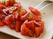 Close-up of watermelon salad with onions and serrano peppers on a rectangular plate with a linen texture