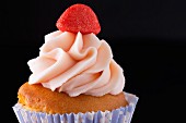 A cupcake decorated with strawberry cream and a strawberry bonbon
