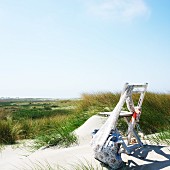 Holz-Klappstuhl mit drapiertem Schal und Badetasche im Sand; Blick in weite Dünenlandschaft