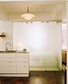 Küchenzeile mit weissen Fronten und Edelstahl-Arbeitsfläche vor Schiebeelementen aus satiniertem Glas