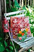 Kissen, Laterne & Krug mit Blumenstrauss auf altem Gartenstuhl
