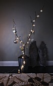 Branch in metal container decorated with string of fairy lights and silver Christmas baubles
