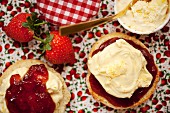 A scone split in half topped with clotted cream and strawberry jam