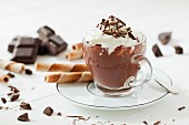 A cup of hot chocolate topped with cream and grated chocolate along with broken chocolate and wafer curls