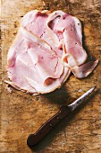 Slices of ham on an old chopping board with a knife