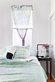 Schlafzimmer in blassen Farben, Bett vor dem Fenster mit Tuch