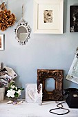 Foto mit weißem Bilderrahmen und Spiegel an Wand, auf rustikalem Holztisch vergoldeter Holzrahmen und diverse Vintage Objekte