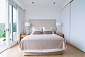 Helles Schlafzimmer mit Doppelbett und Einbauschrank mit weißen Schiebetüren, geöffneten Terrassentüren und Landschaftsblick