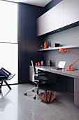 Eingebauter Designer Arbeitsplatz mit Bürostuhl und orangefarbener Retro-Schreibtischlampe vor raumhoher Verglasung