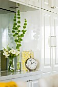 White-painted fitted cupboard with mirrored niche decorated with various vases and antique alarm clock with Roman numerals