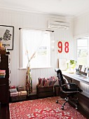 Bright study area with black office chair and red patterned rug in renovated country house with white-painted wood cladding