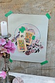 Delicate collage of nostalgic motifs fixed on concrete wall with washi tape; silver candlestick with hydrangea flowers