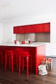 Crate of apples and bag on floor next to island counter with red-painted beech veneer and bar stools