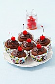 Chocolate muffins decorated with chocolate glaze and cocktail cherries
