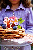 A girl holding a plate of waffles with plums and colourful paper mushrooms