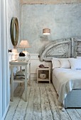 Französisches Bett mit antikem Kopfteil vor weißer Wandverkleidung, graublauer Vintage Wand und verwittertem Dielenboden